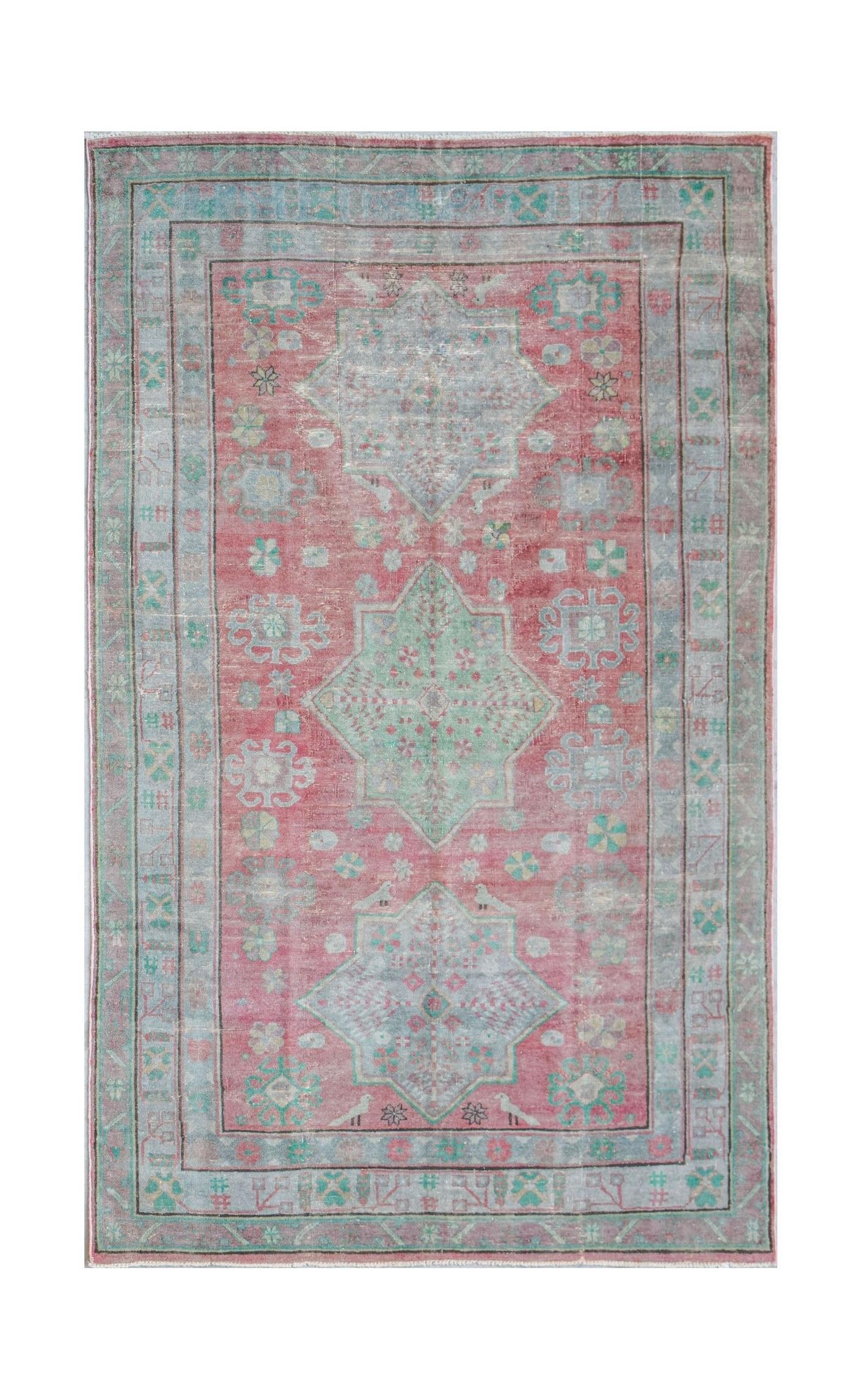 A vintage handwoven Persian rug featuring a pink field with geometric medallions in blue and green.