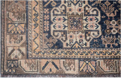 A vintage handmade Persian wool rug featuring a dark blue central medallion and tribal patterns.