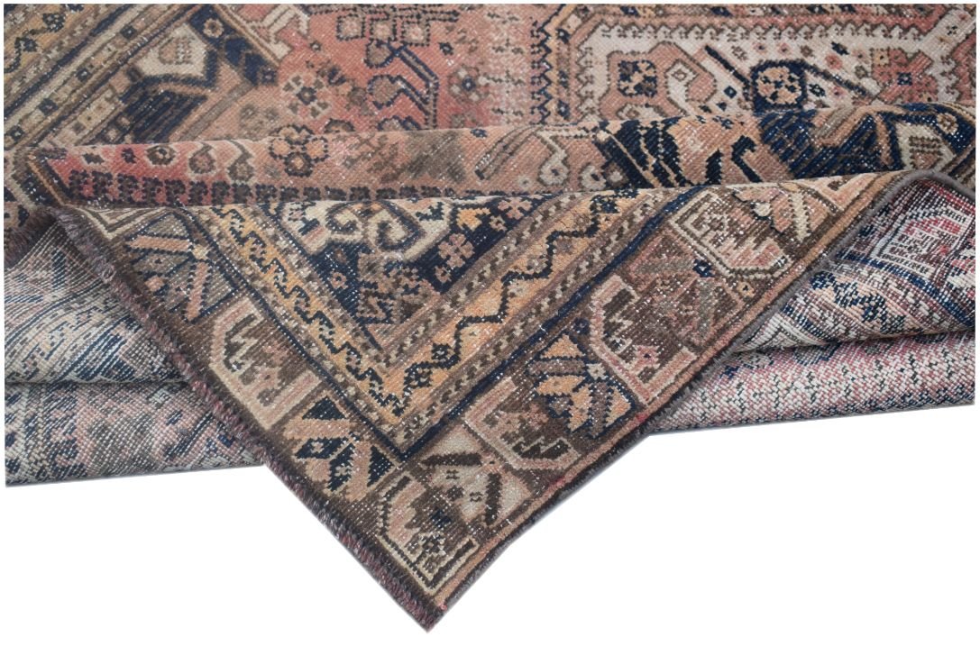 A folded vintage Persian wool rug featuring intricate tribal patterns in muted pink and blue tones.