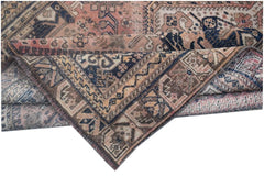 A folded vintage Persian wool rug featuring intricate tribal patterns in muted pink and blue tones.