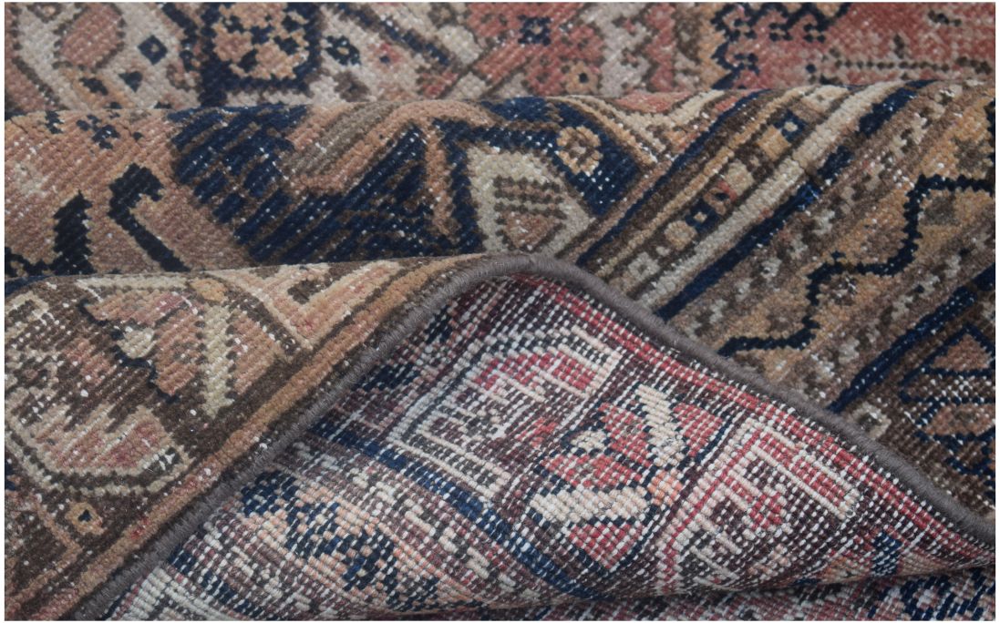 A folded vintage Persian wool rug featuring intricate tribal patterns in muted earth tones.