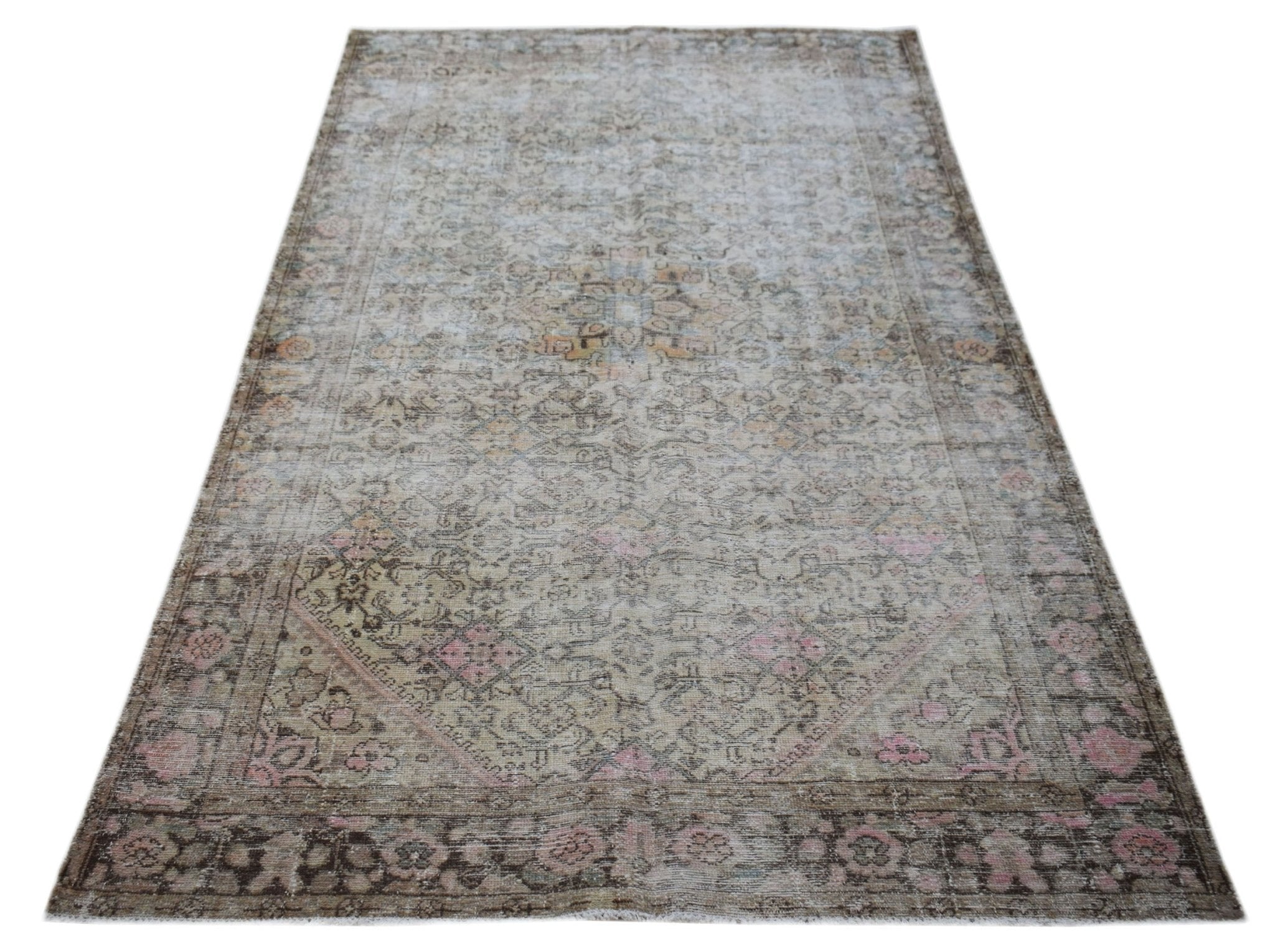 A vintage handwoven Persian rug featuring a faded floral pattern in muted tones of pink and brown.