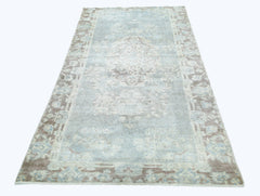 A vintage Persian rug featuring a faded blue and beige floral medallion pattern.