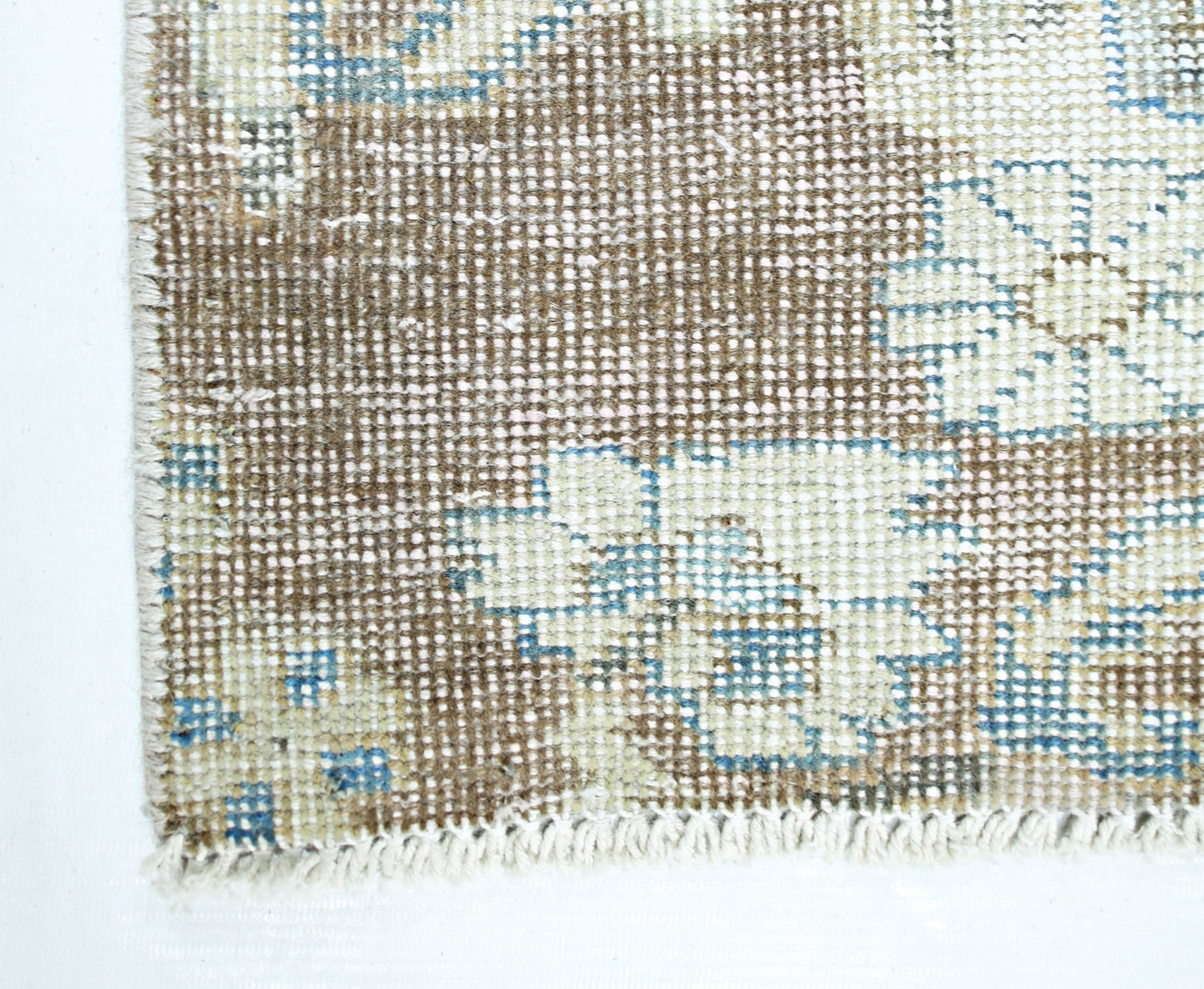 A close-up of a vintage Persian rug featuring a faded floral pattern in brown, blue, and cream.