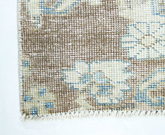 A close-up of a vintage Persian rug featuring a faded floral pattern in brown, blue, and cream.