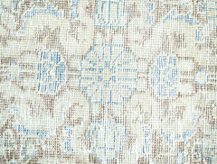 A close-up view of a vintage Persian rug featuring a faded floral pattern in blue and brown tones.