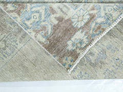 A folded corner of a vintage Persian rug showing a blue and brown floral pattern on wool.