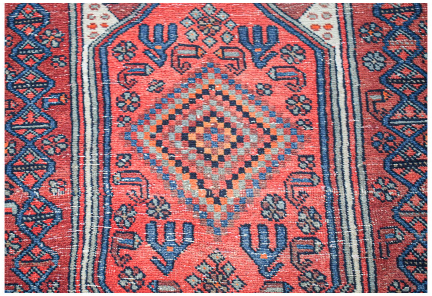 A vintage handwoven Persian rug featuring a central diamond motif in red, blue, and orange tones.