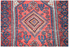 A vintage handwoven Persian rug featuring a central diamond motif in red, blue, and orange tones.