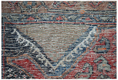 A close-up of a handwoven vintage Persian rug featuring a geometric pattern in red, blue, and tan.