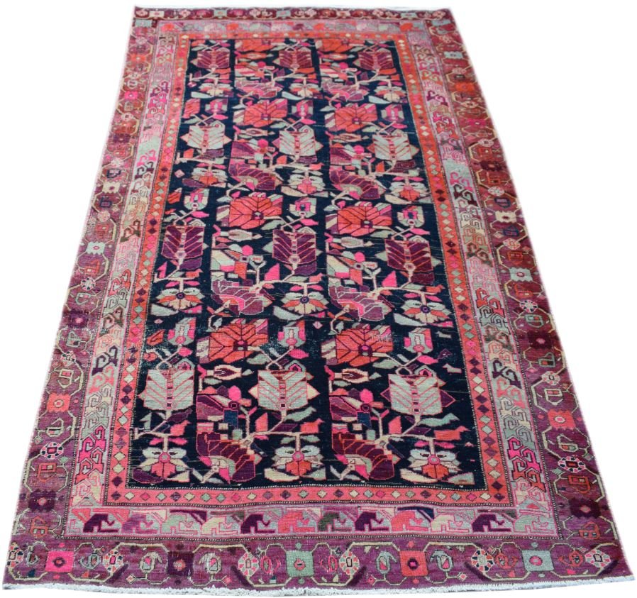 A vintage handmade Persian wool rug featuring a dark field with colorful floral and tribal motifs.