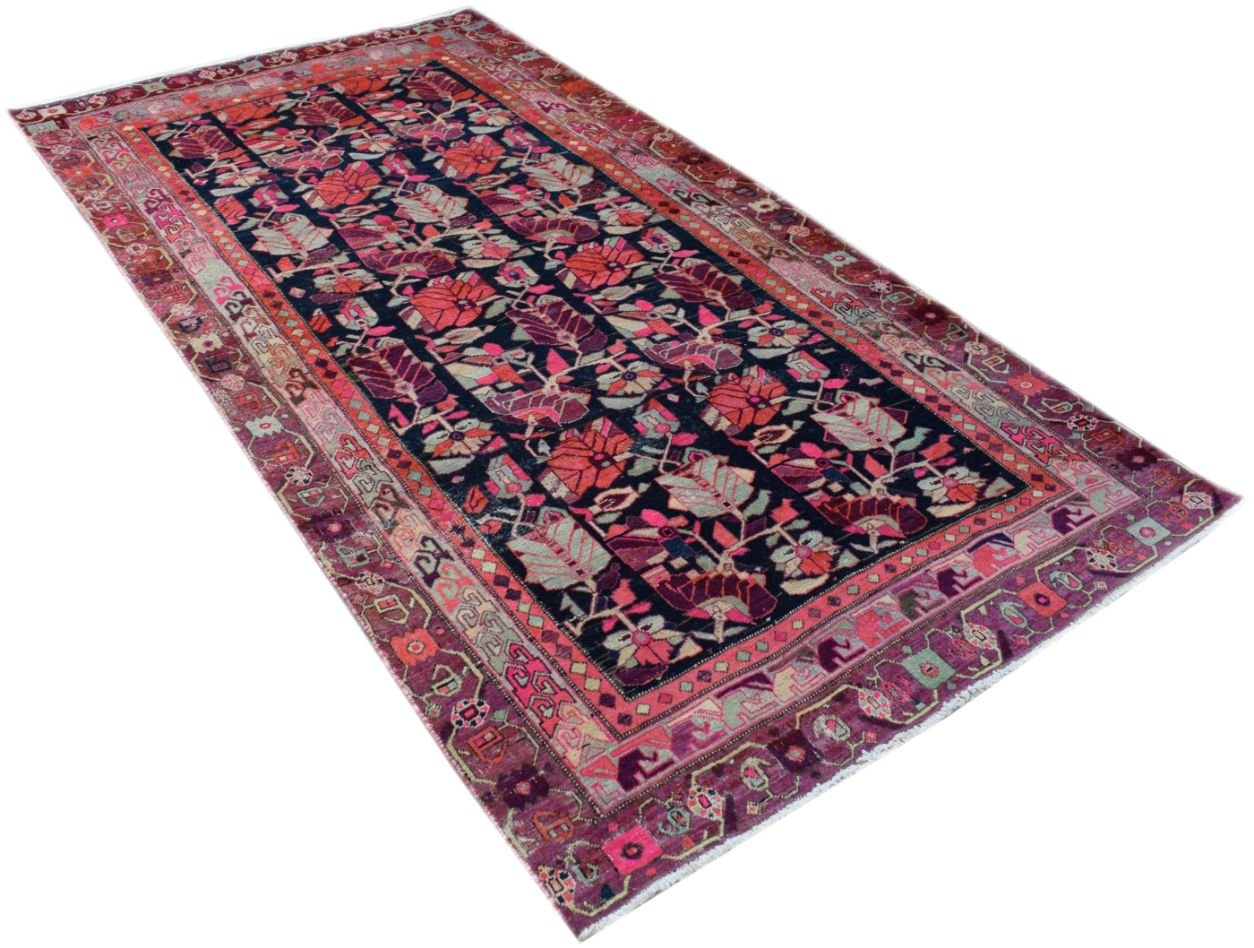 A rectangular vintage Persian rug featuring a dark field with vibrant floral and tribal patterns.