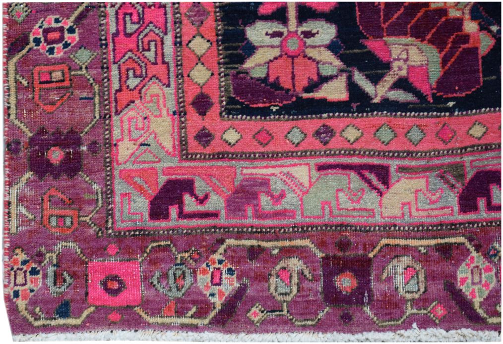 A vintage handmade Persian rug featuring geometric floral patterns in shades of pink and purple.