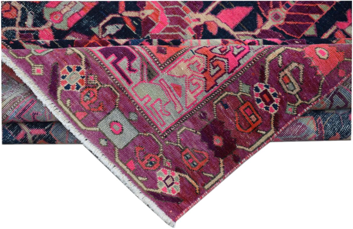 A folded vintage Persian wool rug featuring intricate tribal patterns in vibrant pink and purple.