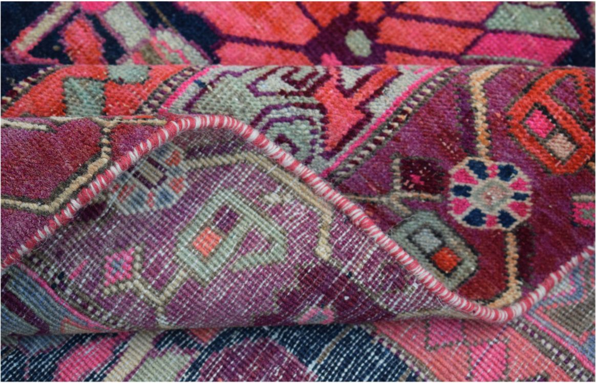 A folded vintage Persian rug featuring intricate geometric patterns in vibrant pink and purple tones.
