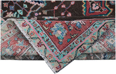A folded vintage Persian wool rug featuring a dark brown field and a colorful floral border.