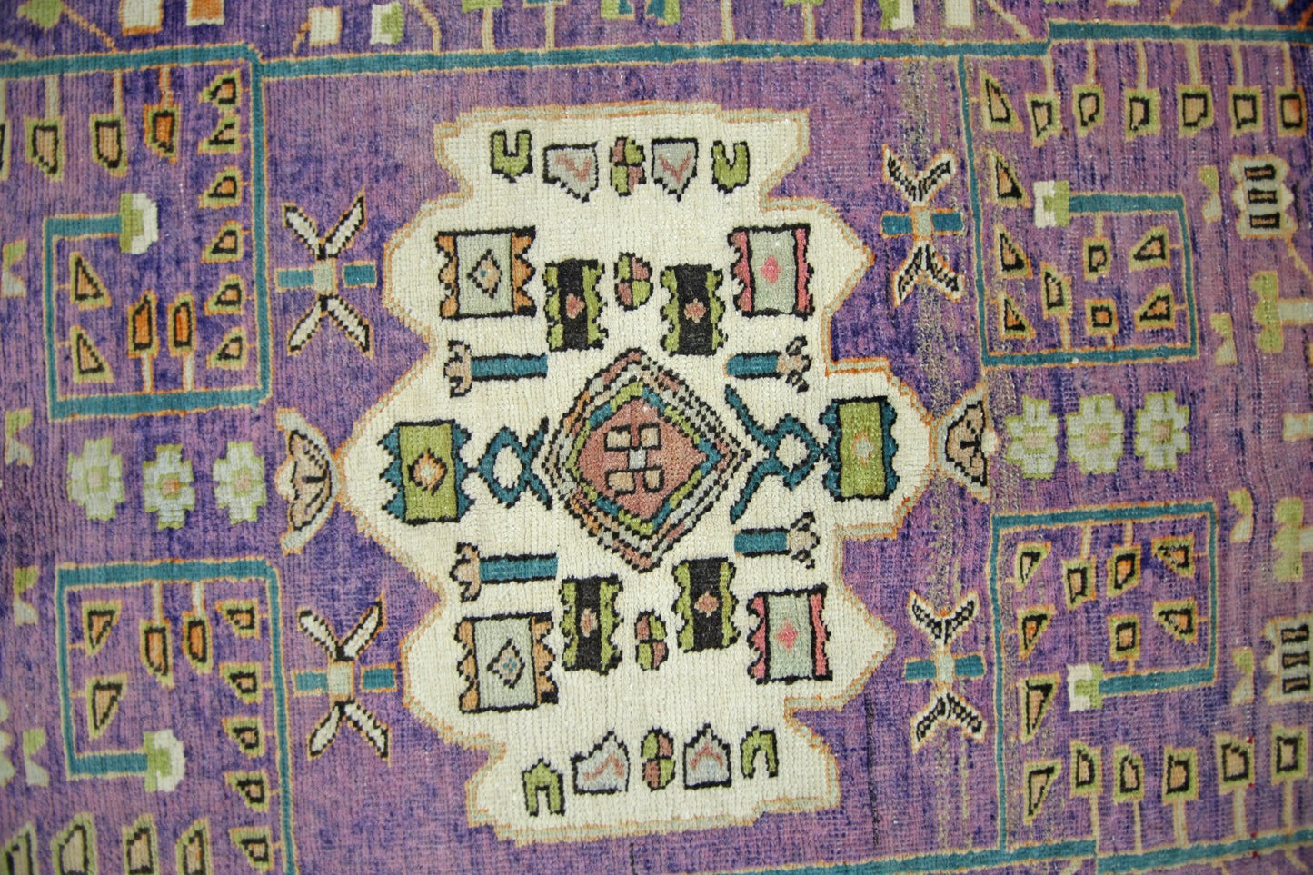 A vintage handmade Persian rug featuring a central geometric medallion on a vibrant purple field.