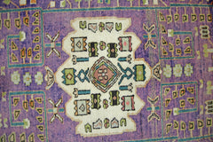 A vintage handmade Persian rug featuring a central geometric medallion on a vibrant purple field.