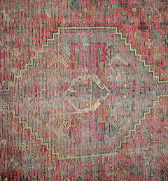 A vintage Persian rug featuring a faded geometric medallion pattern in red and grey tones.