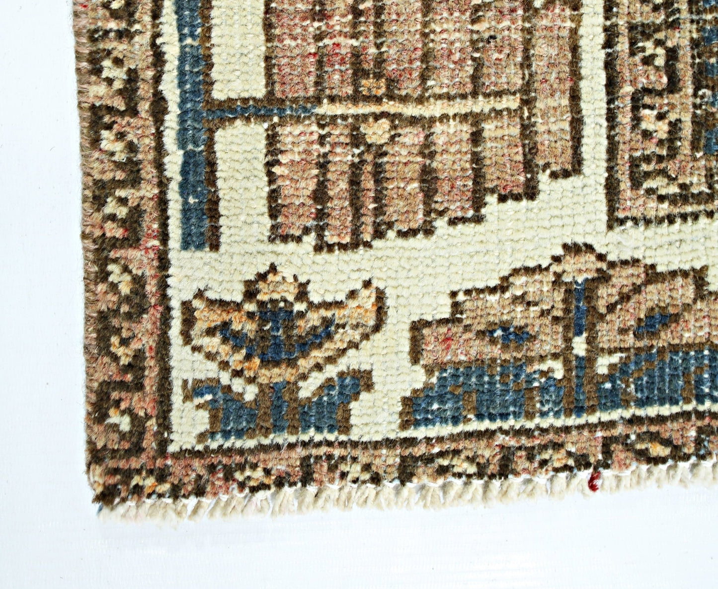 A close-up of a vintage Persian rug featuring geometric floral patterns in blue and tan wool.