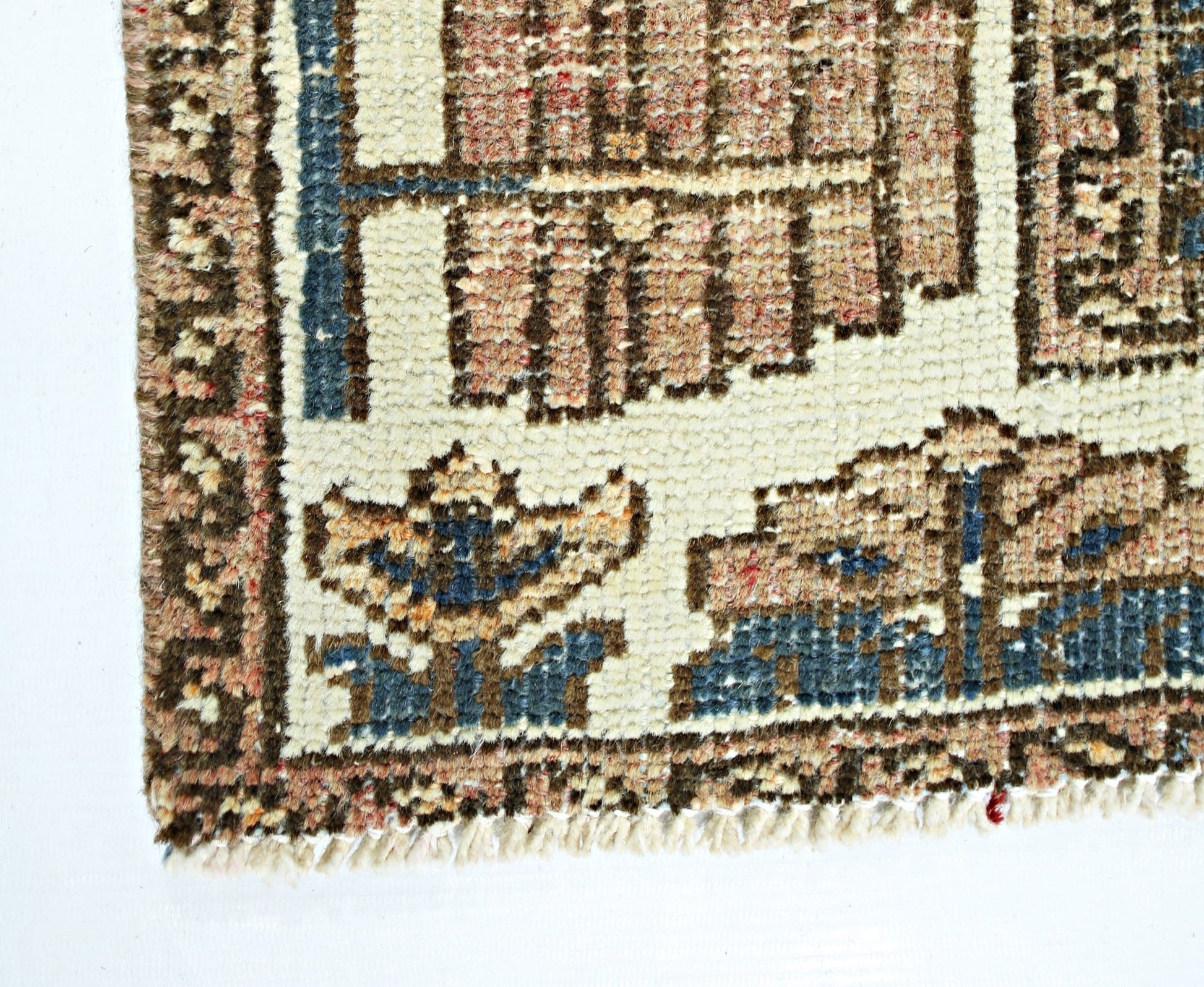 A close-up of a vintage Persian rug featuring geometric floral patterns in blue and tan wool.