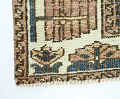 A close-up of a vintage Persian rug featuring geometric floral patterns in blue and tan wool.