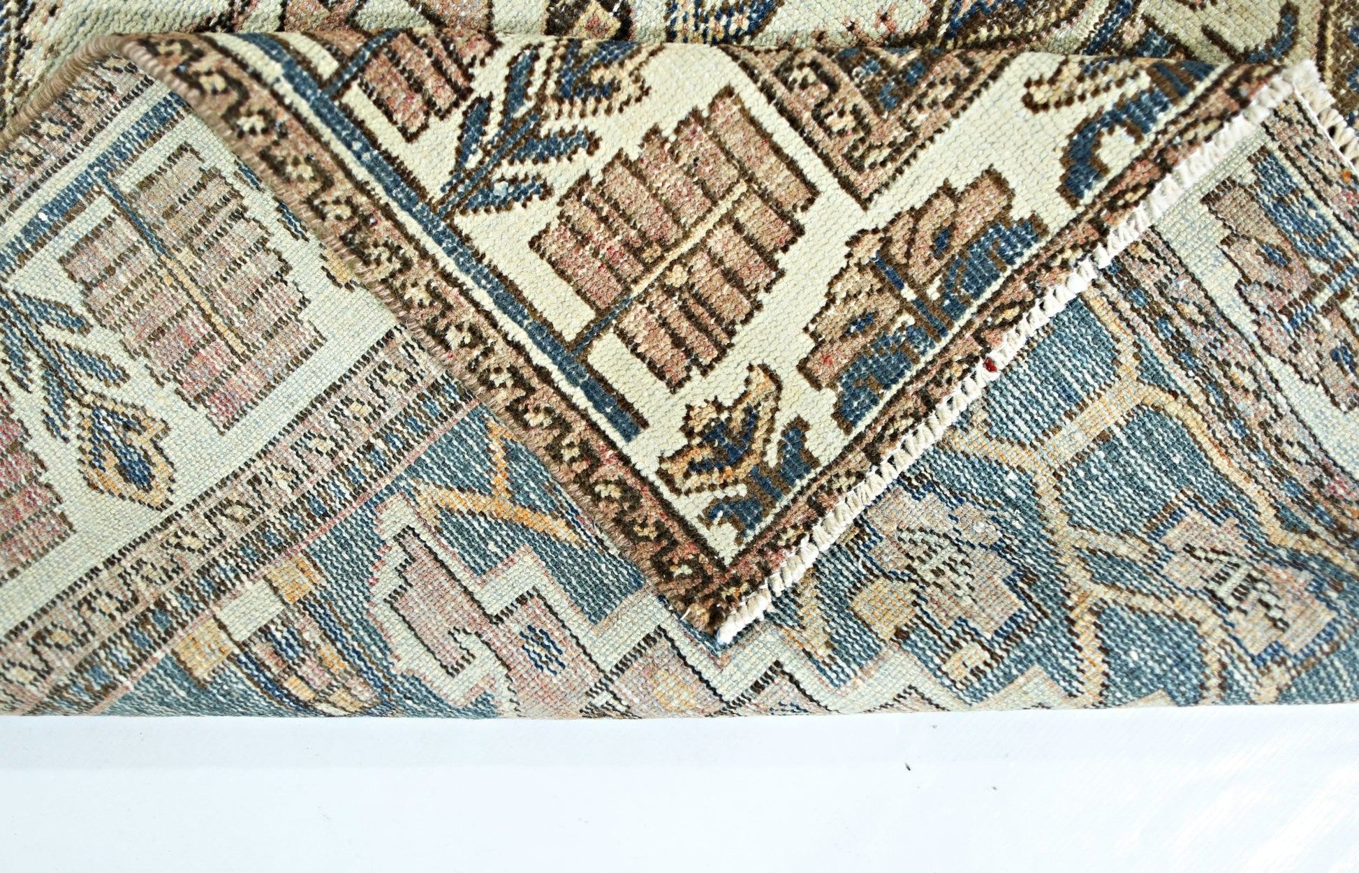 A folded corner of a vintage handmade Persian rug featuring intricate geometric patterns in blue and tan.