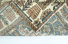 A folded corner of a vintage handmade Persian rug featuring intricate geometric patterns in blue and tan.