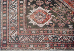 A handmade vintage Persian wool rug featuring a dark green field with a central geometric medallion.