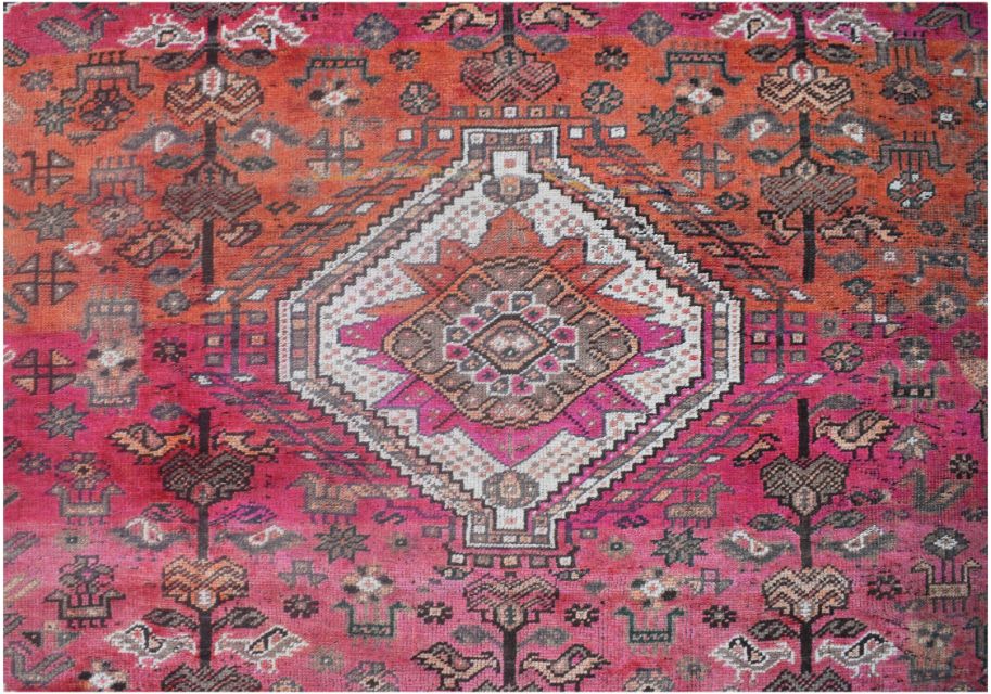 A handmade vintage Persian wool rug featuring a central diamond medallion on a vibrant pink field.