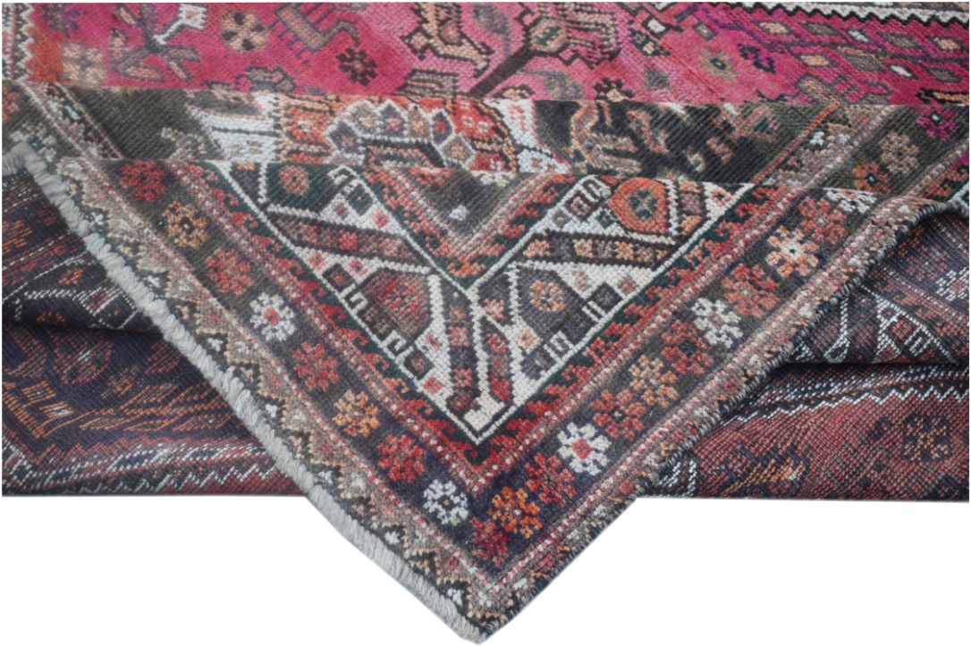 A folded vintage Persian wool rug featuring intricate tribal patterns in pink and dark tones.