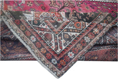 A folded vintage Persian wool rug featuring intricate tribal patterns in pink and dark tones.