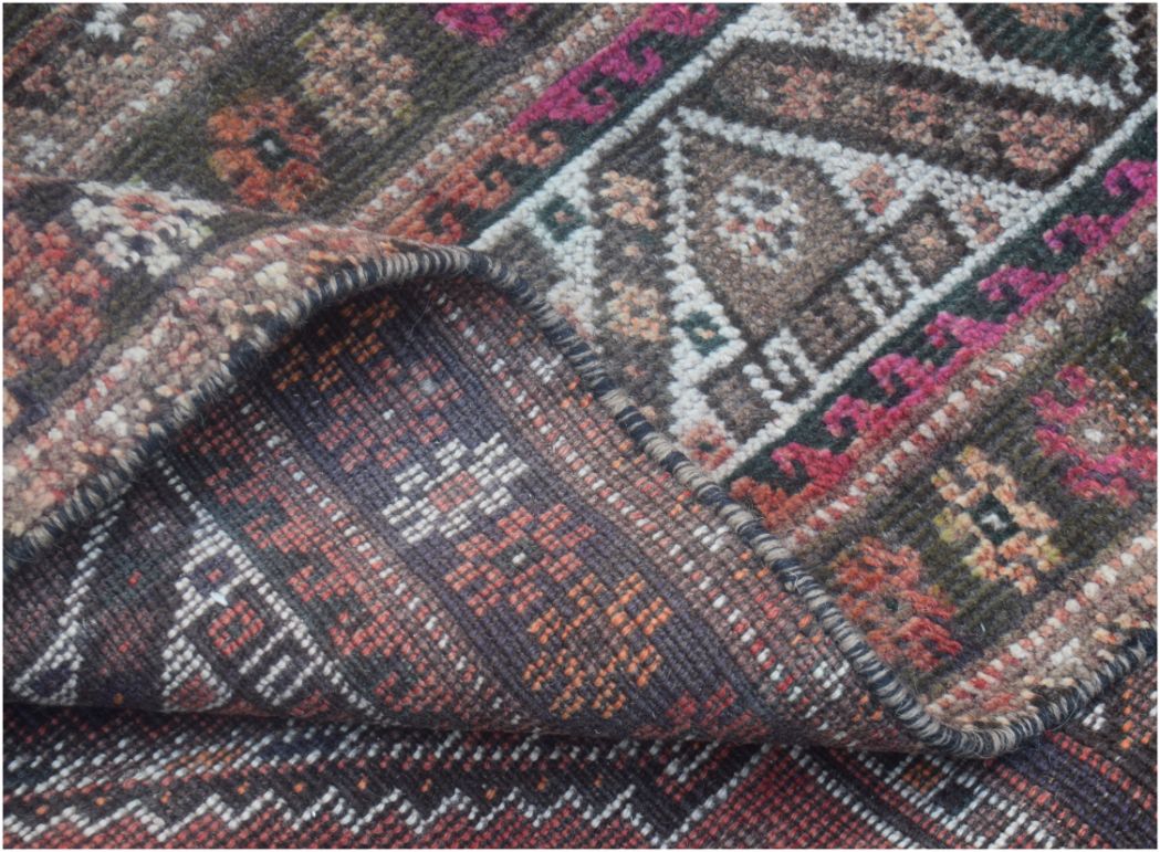 A folded corner of a handmade vintage Persian wool rug featuring intricate tribal patterns.