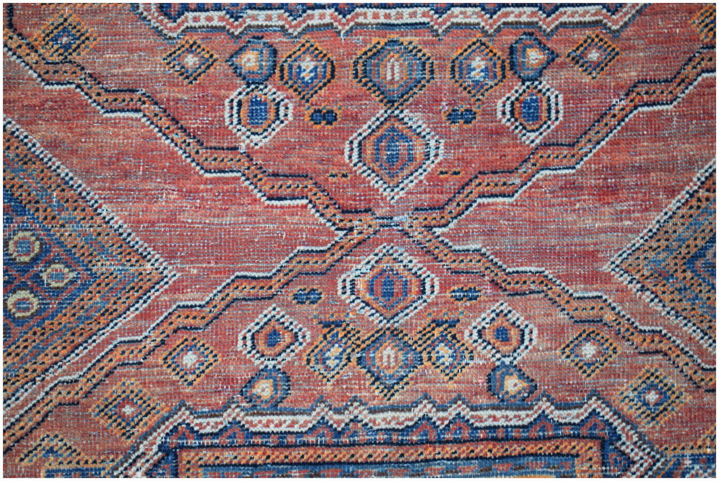 A vintage handwoven Persian rug featuring a geometric pattern in shades of red, blue, and orange.