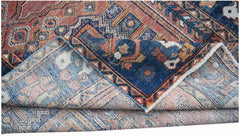 A handwoven vintage Persian rug with a folded corner revealing its intricate blue and red pattern.