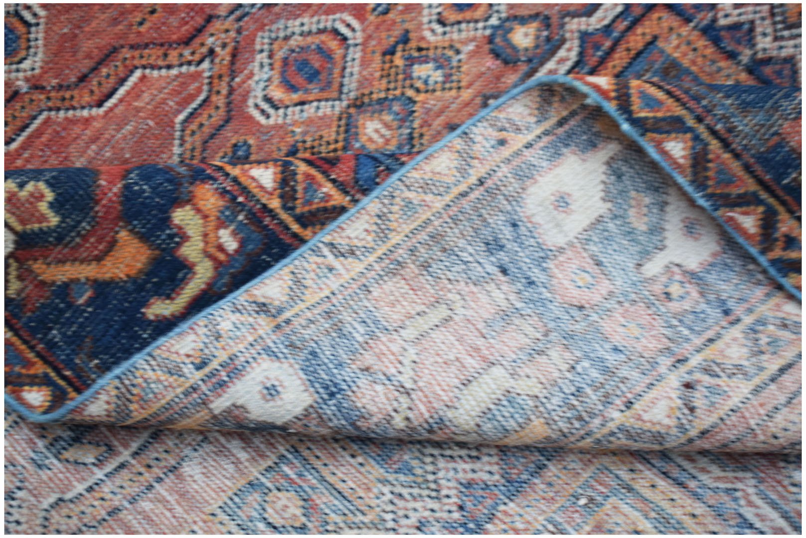 A vintage handwoven Persian rug with a folded corner revealing its intricate red and blue pattern.