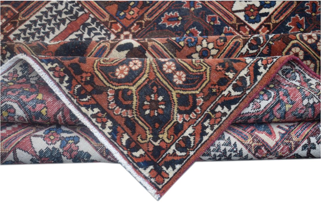 A folded vintage Persian wool rug featuring intricate tribal patterns in red, blue, and cream.