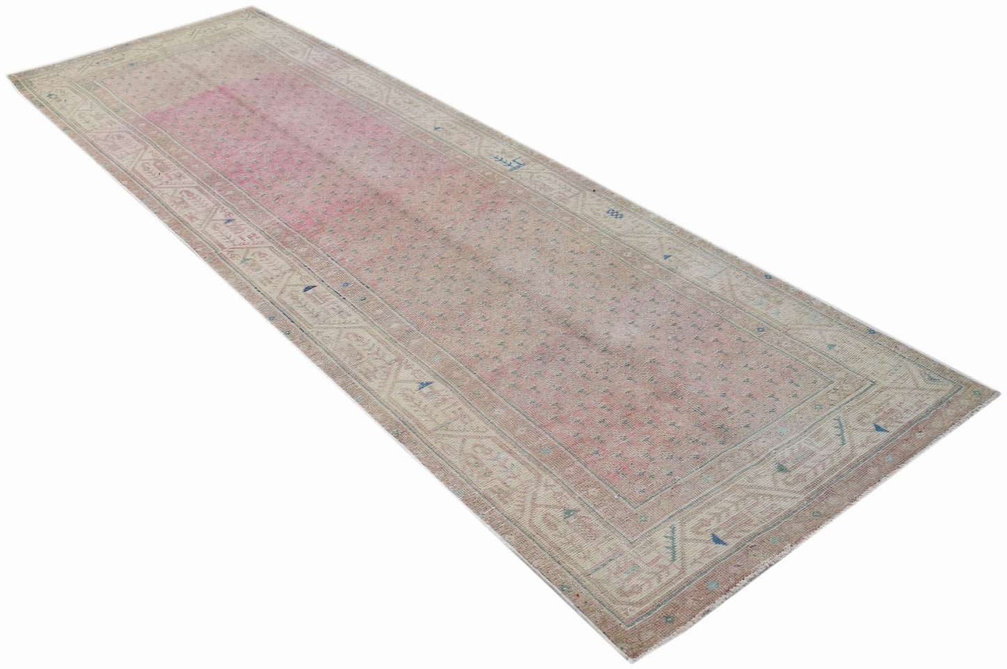 A long, handwoven vintage Persian runner rug featuring a faded pink center and neutral borders.