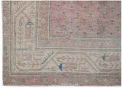 A vintage handwoven Persian rug featuring a faded pink field with blue floral accents and borders.