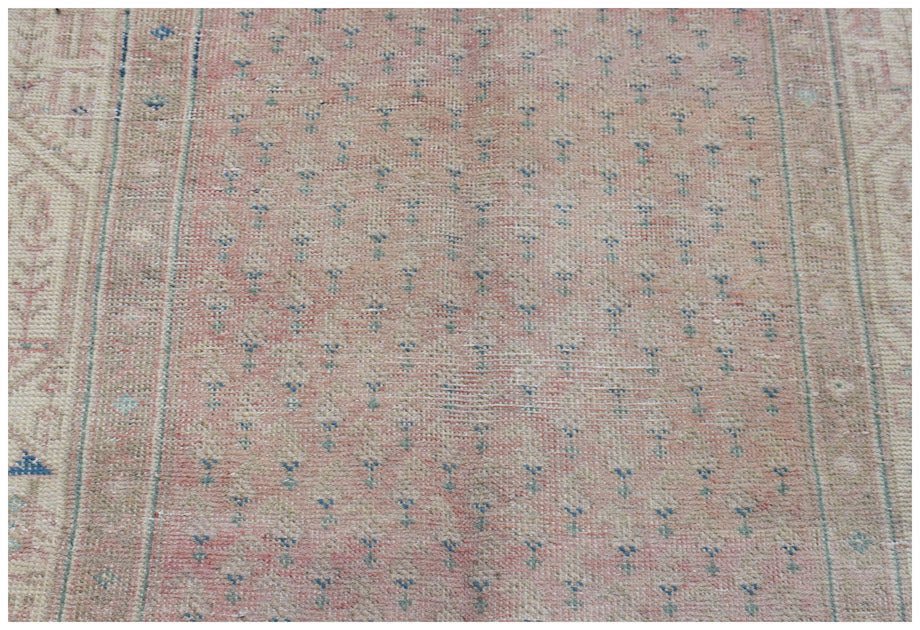 A vintage handwoven Persian rug featuring a faded pink field with a repeating blue floral pattern.