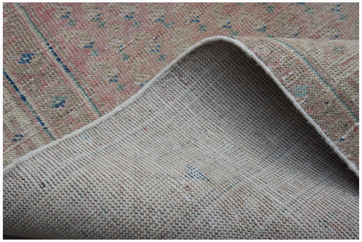 A vintage Persian rug with a faded pink and beige pattern, shown folded to reveal its woven back.