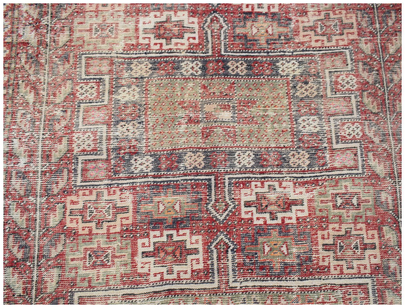 A vintage handwoven Persian rug featuring a geometric pattern in red, blue, and cream tones.