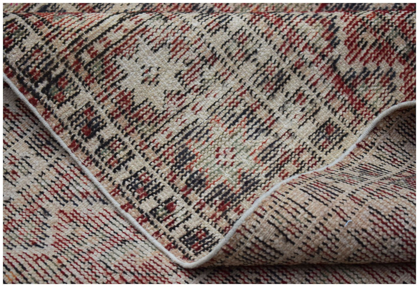 A folded vintage Persian rug featuring a distressed geometric pattern in red, black, and beige.