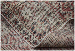 A folded vintage Persian rug featuring a distressed geometric pattern in red, black, and beige.
