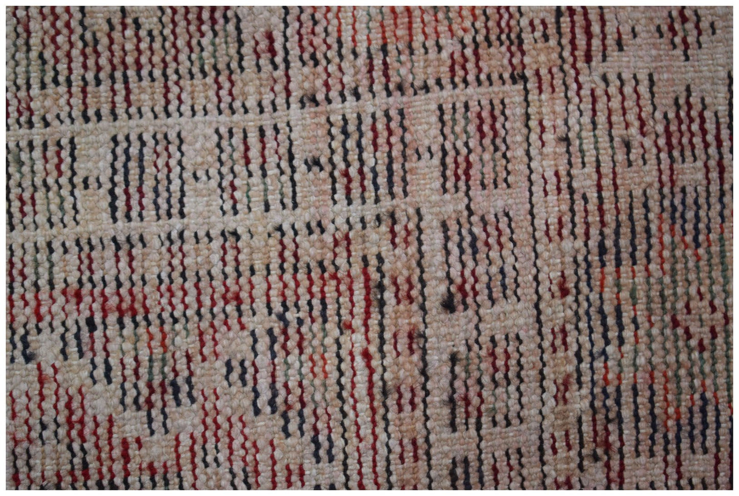 A close-up of a vintage handwoven Persian rug featuring a textured pattern of red and blue stripes.