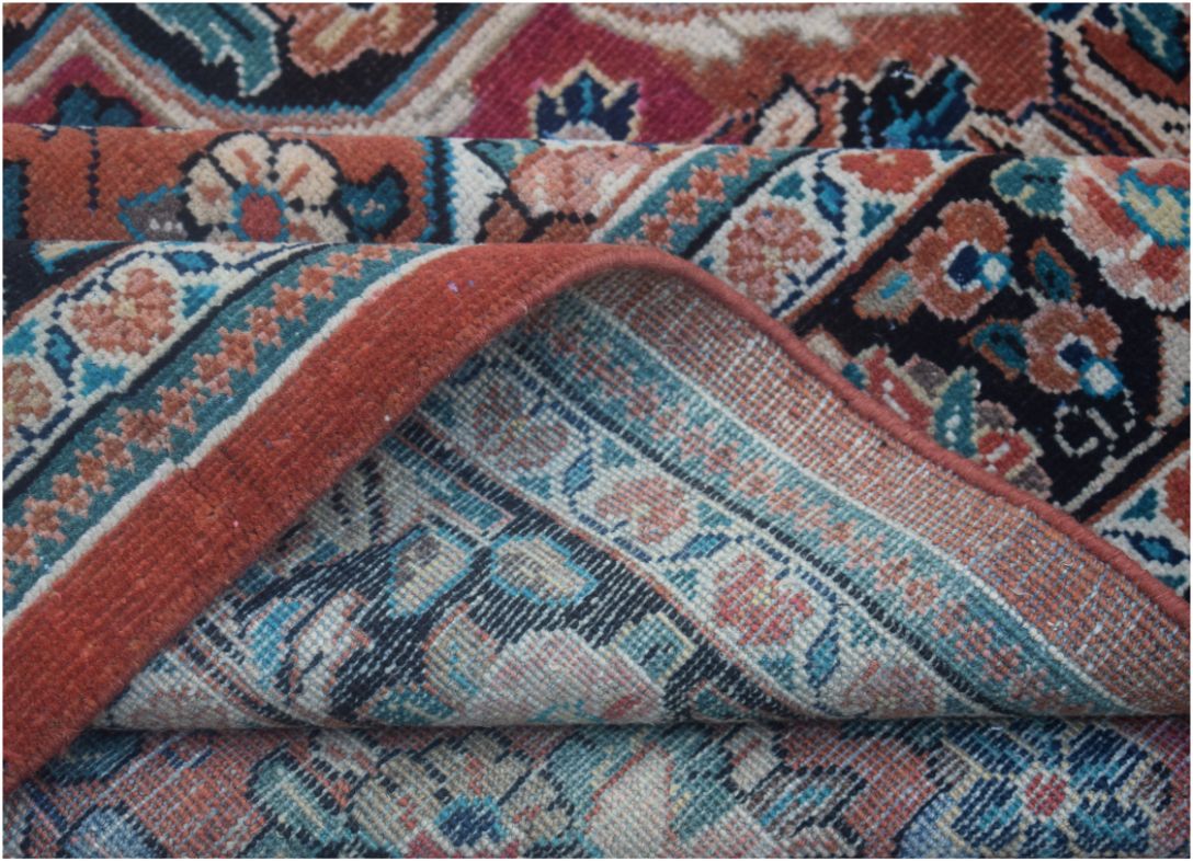 A corner of a handmade vintage Persian wool rug is folded back to reveal its woven underside.