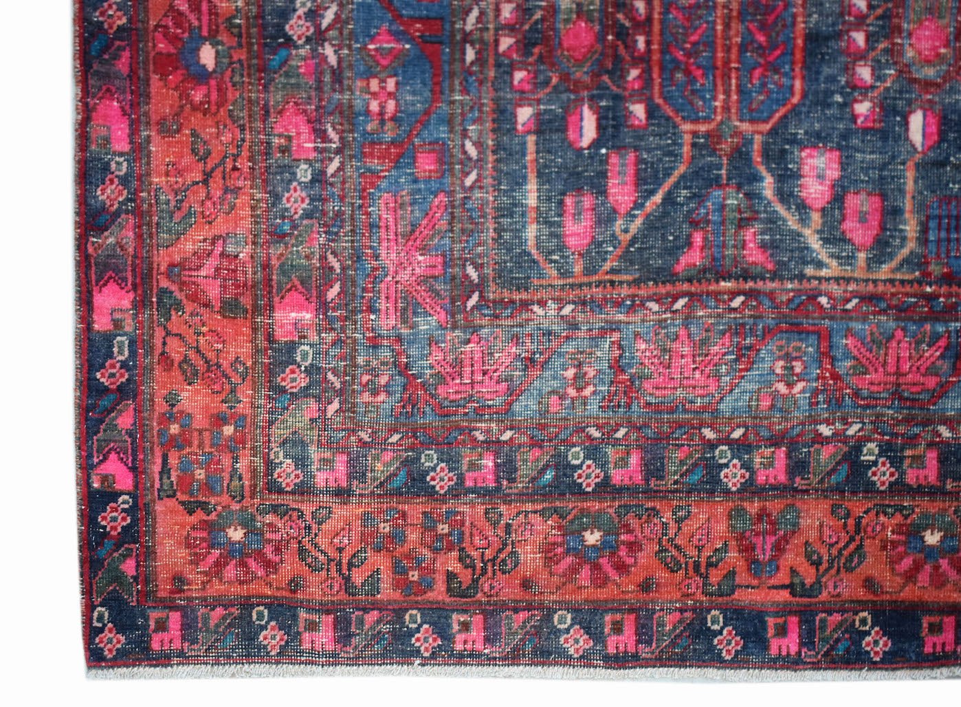 A vintage handwoven Persian rug featuring a floral pattern in shades of blue and pink.