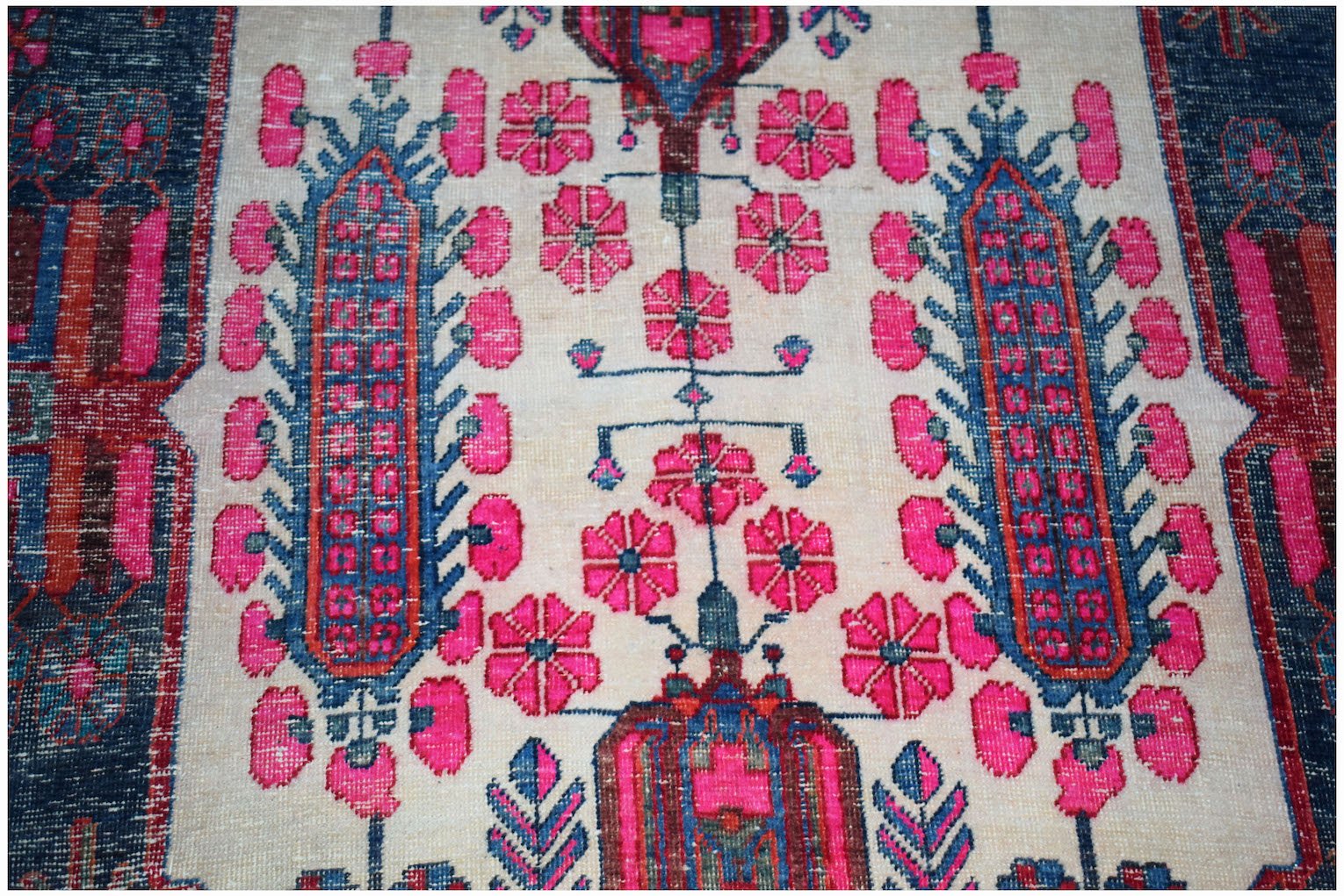 A vintage handwoven Persian rug featuring a floral pattern in vibrant pink and blue on a cream base.