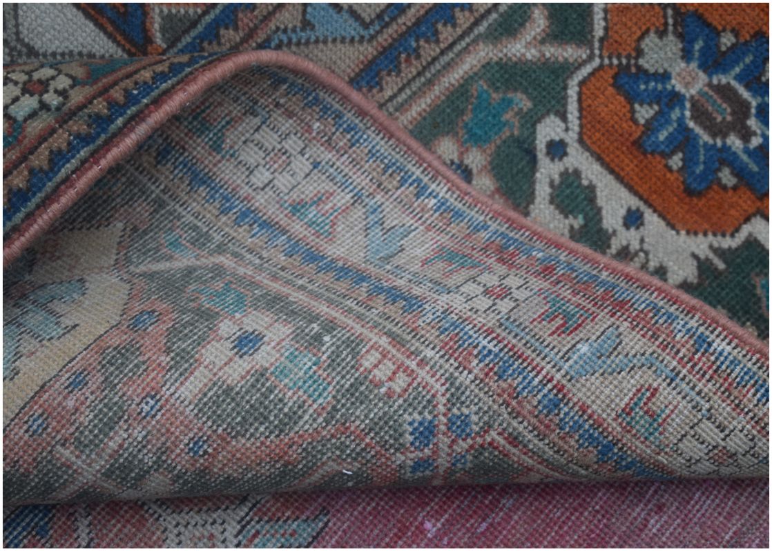A corner of a vintage Persian wool rug is folded back to reveal its intricate floral pattern.
