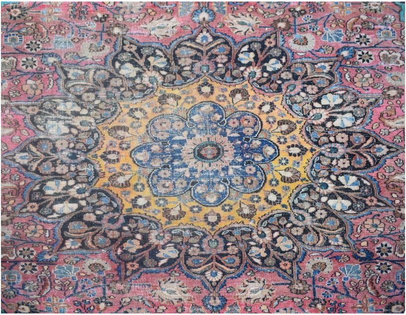 A vintage handmade Persian wool rug featuring a central floral medallion on a pink background.